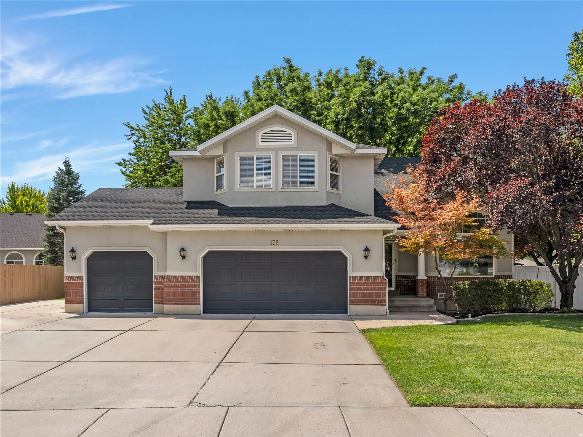 Stucco exterior with brick accents, featuring a dual garage with dark doors, a concrete driveway, and mature landscaping