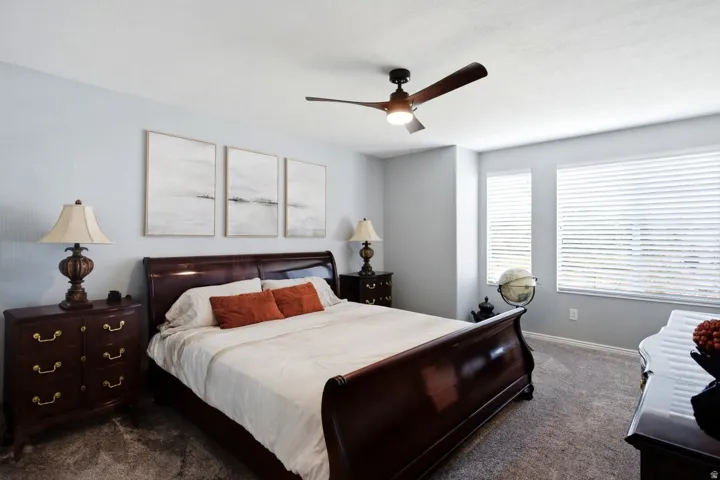 Carpeted bedroom featuring multiple windows with horizontal blinds, a ceiling fan with integrated lighting, and light-toned wall finishes