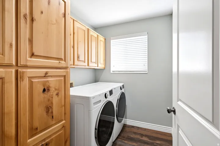 Dedicated laundry area featuring abundant wood cabinetry, wood-finish flooring, and a single window with blinds