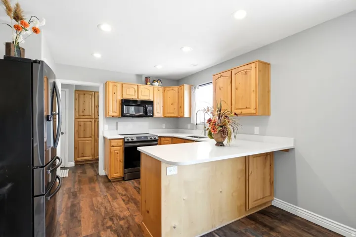 Bright kitchen featuring wood-finish flooring, light wood cabinetry, white countertops, a black microwave, and a black range