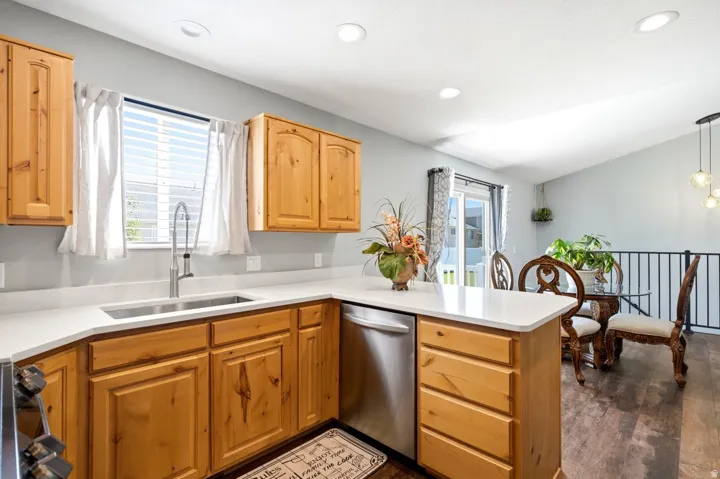 Kitchen featuring wood cabinetry, light-toned countertops, a stainless steel sink with a gooseneck faucet, and integrated stainless steel appliances