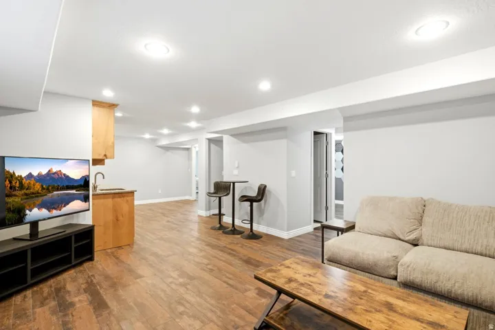 Spacious open-concept room featuring wood-finish flooring, recessed lighting, a built-in wet bar with a stainless steel sink, and light-toned walls