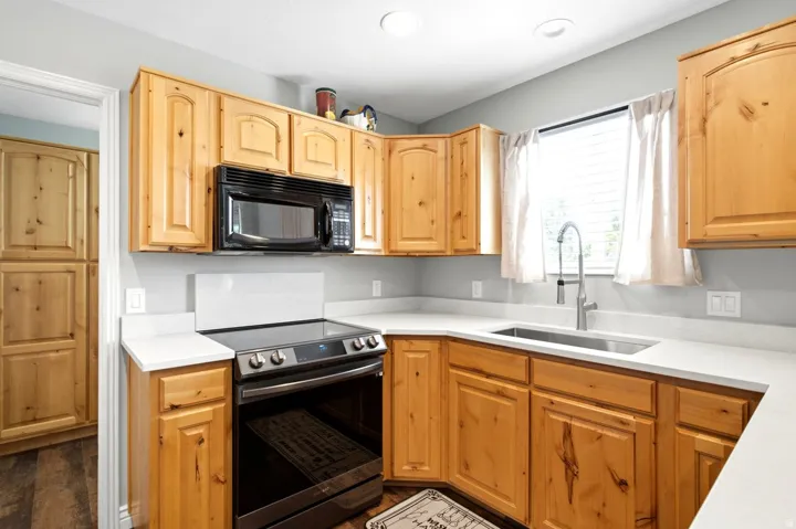 Kitchen featuring natural wood cabinetry, light-toned countertops, stainless steel sink with gooseneck faucet, black electric range, and coordinating built-in microwave