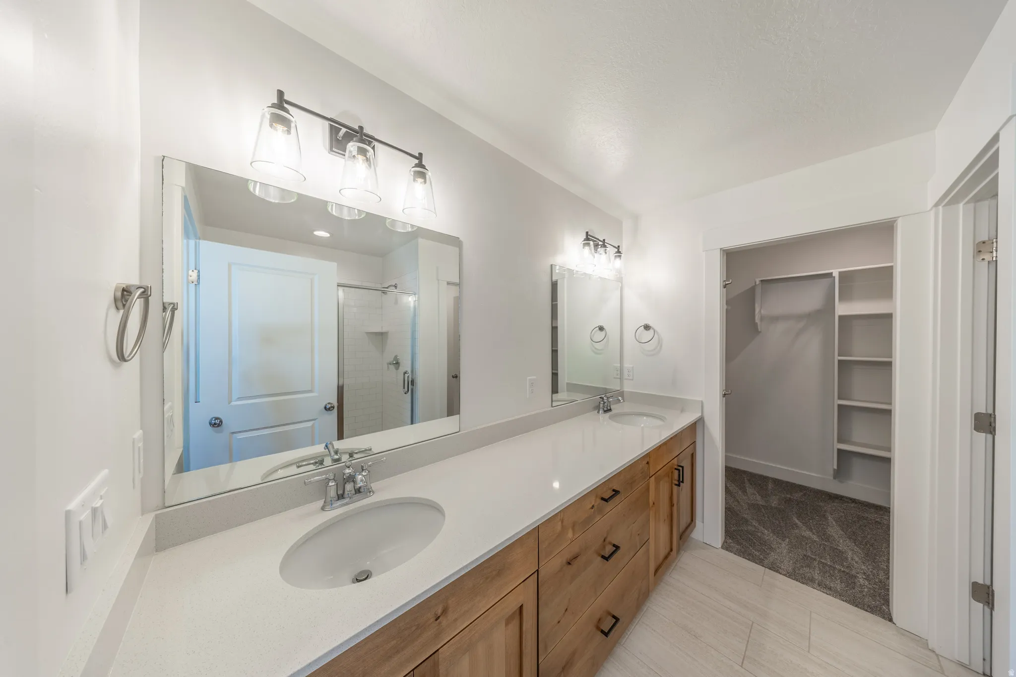 Double vanity with light countertops, wood-finish cabinetry, and contemporary fixtures