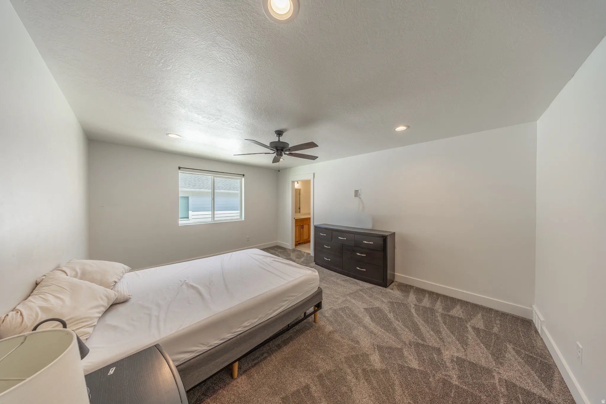 Spacious room featuring patterned carpeting, recessed lighting, a ceiling fan, and a window providing natural light