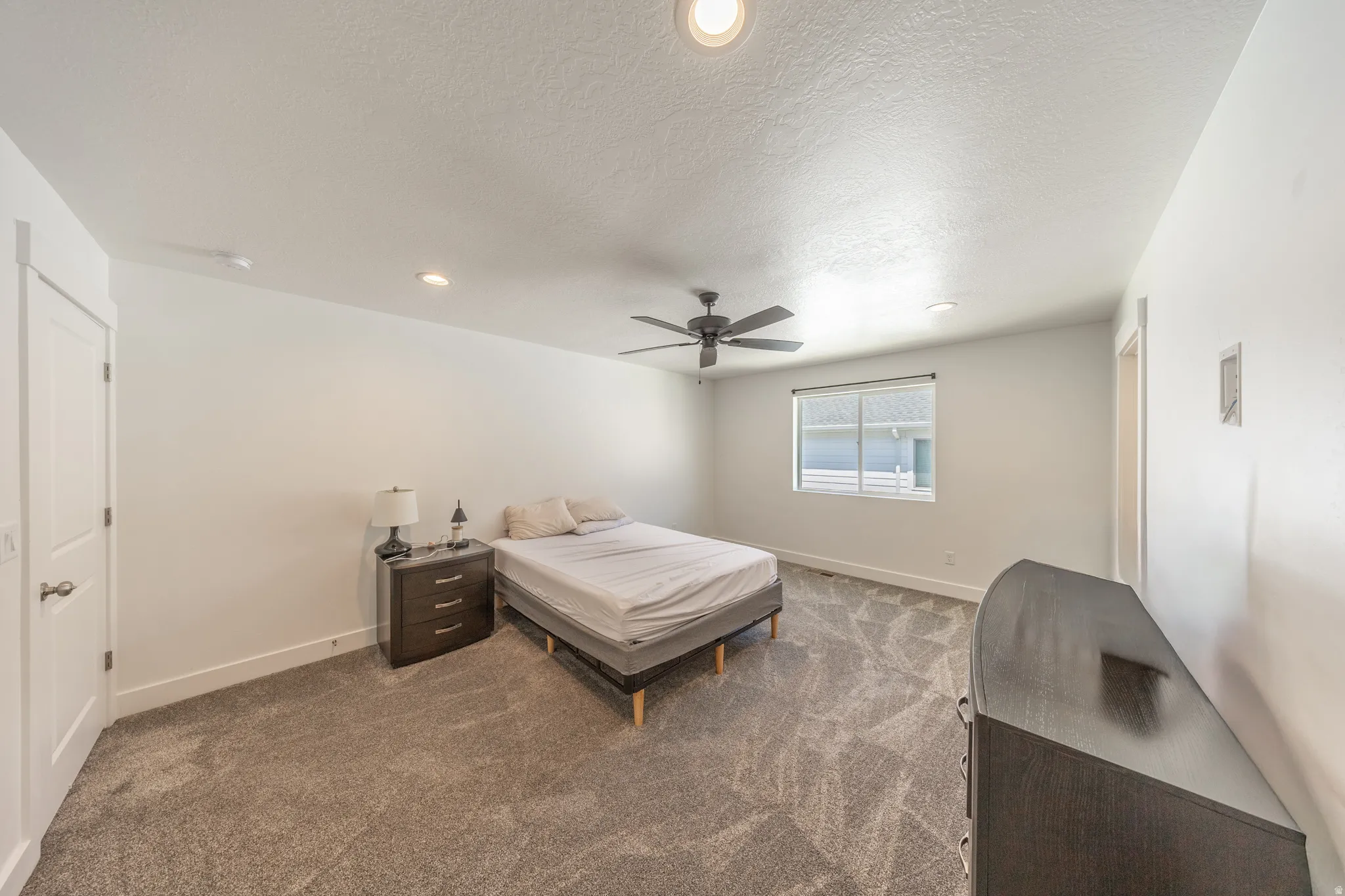 Carpeted room featuring a ceiling fan with integrated lighting, recessed ceiling lights, a large window, and a paneled door
