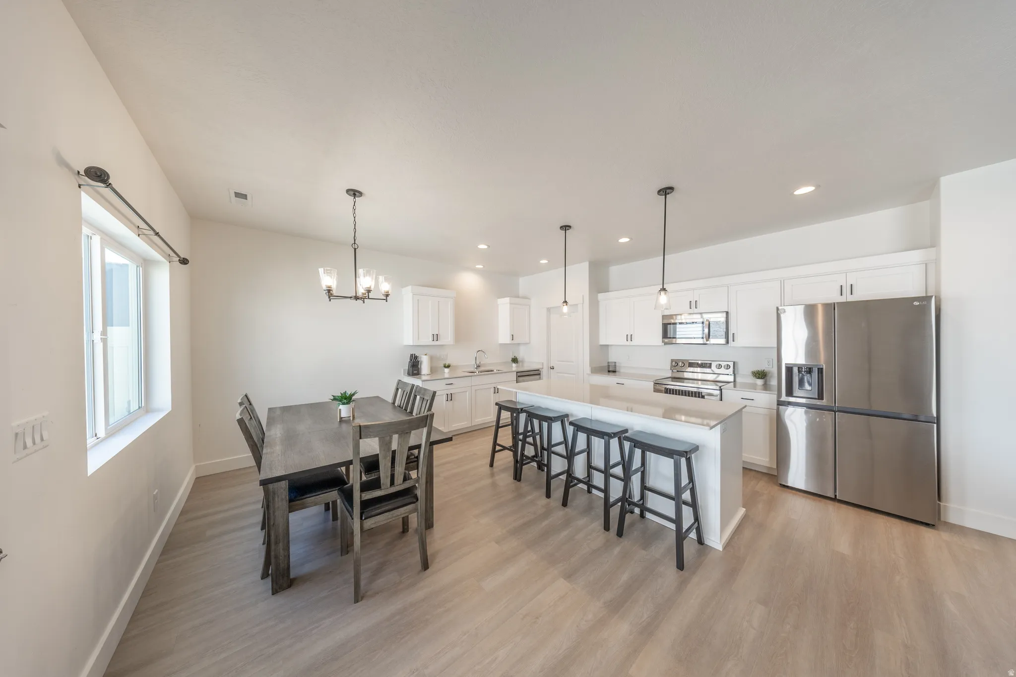 Open-concept kitchen and dining area featuring light wood-finish flooring, white cabinetry, stainless steel appliances, and a central island with bar seating