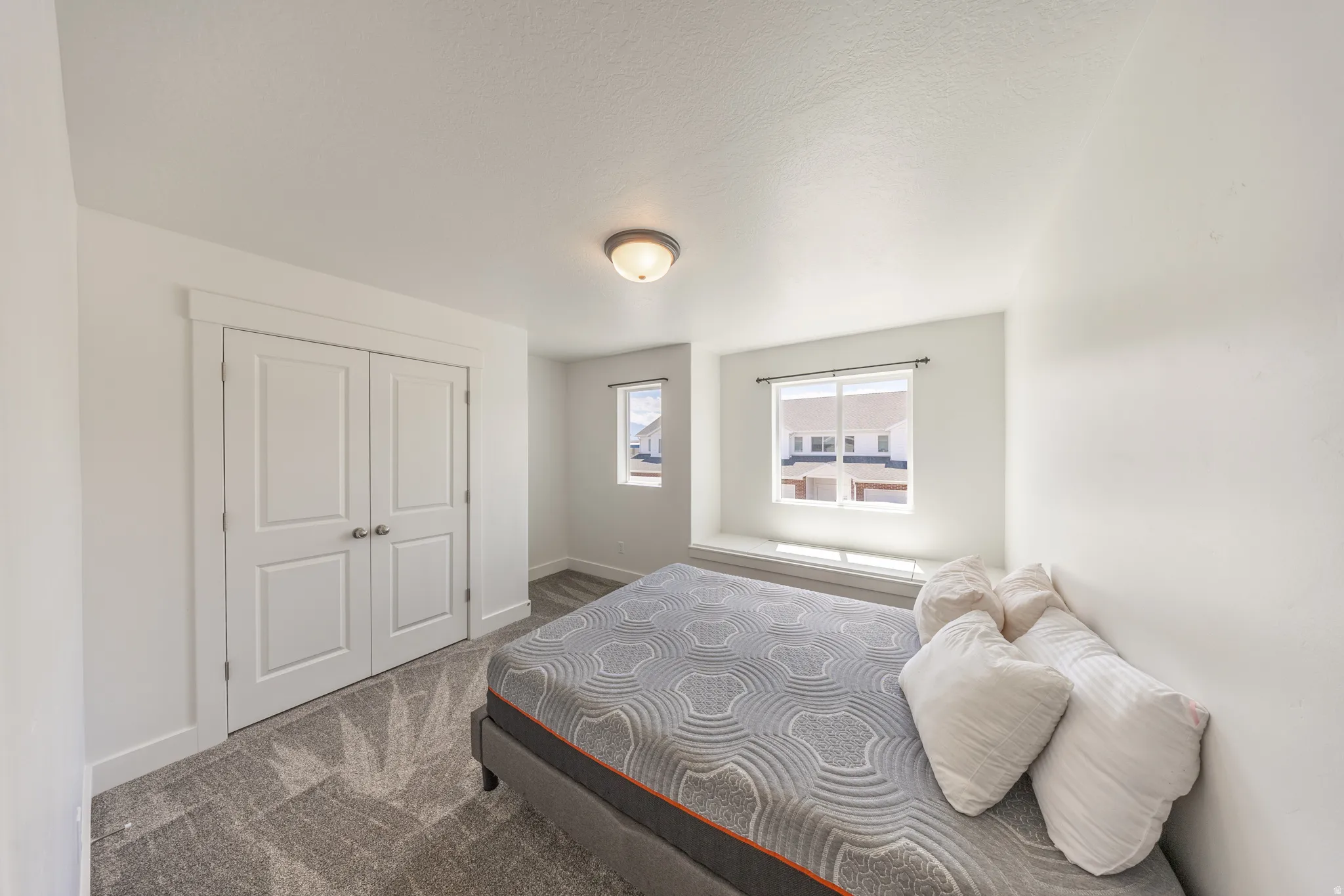 Neutral-toned room featuring a built-in window seat, two panel closet doors, a flush-mount ceiling light fixture, and grey patterned carpeting