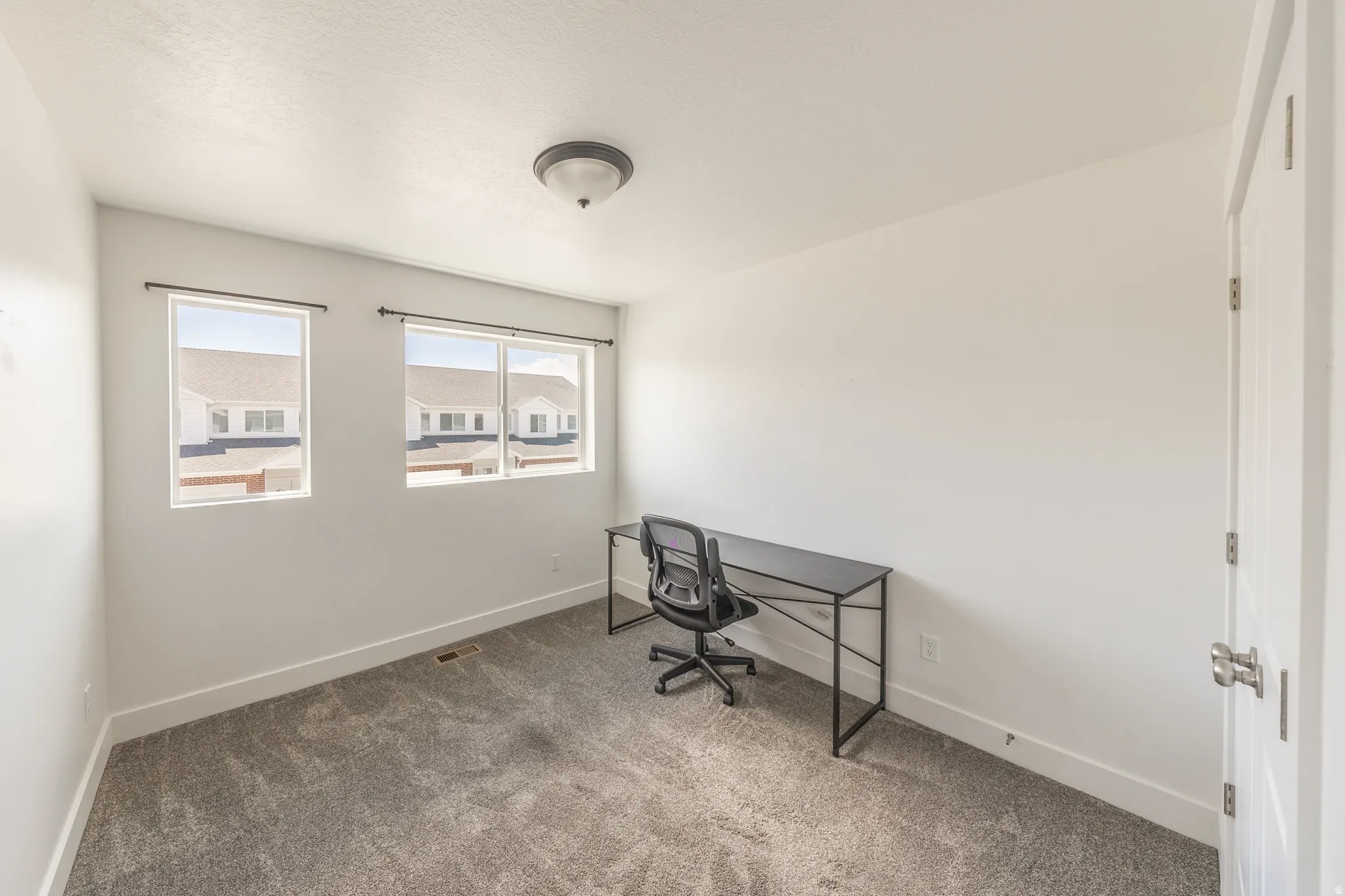 White-painted interior room featuring two windows with black curtain rods, light gray carpet, and a flush-mount ceiling light fixture