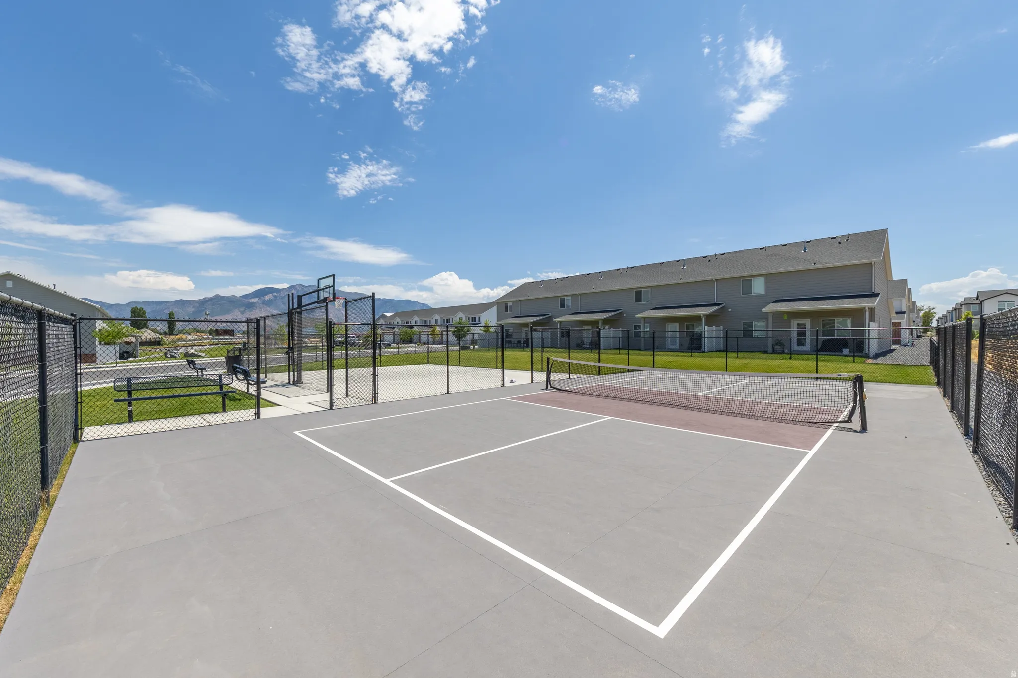Recreational court featuring a pickleball net, basketball hoop, and chain-link fencing