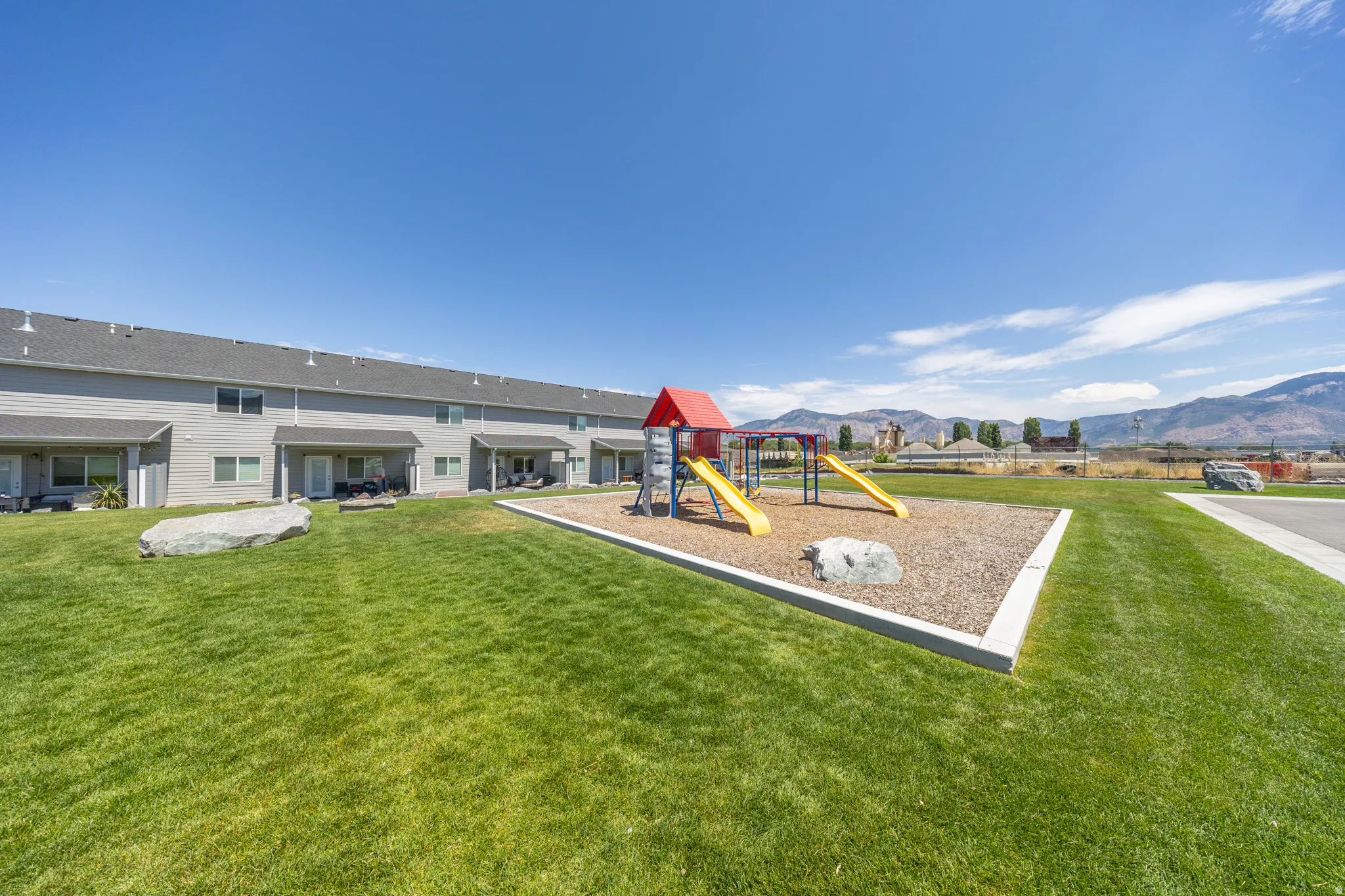Community playground area featuring a red and yellow play structure with slides, surrounded by a manicured lawn