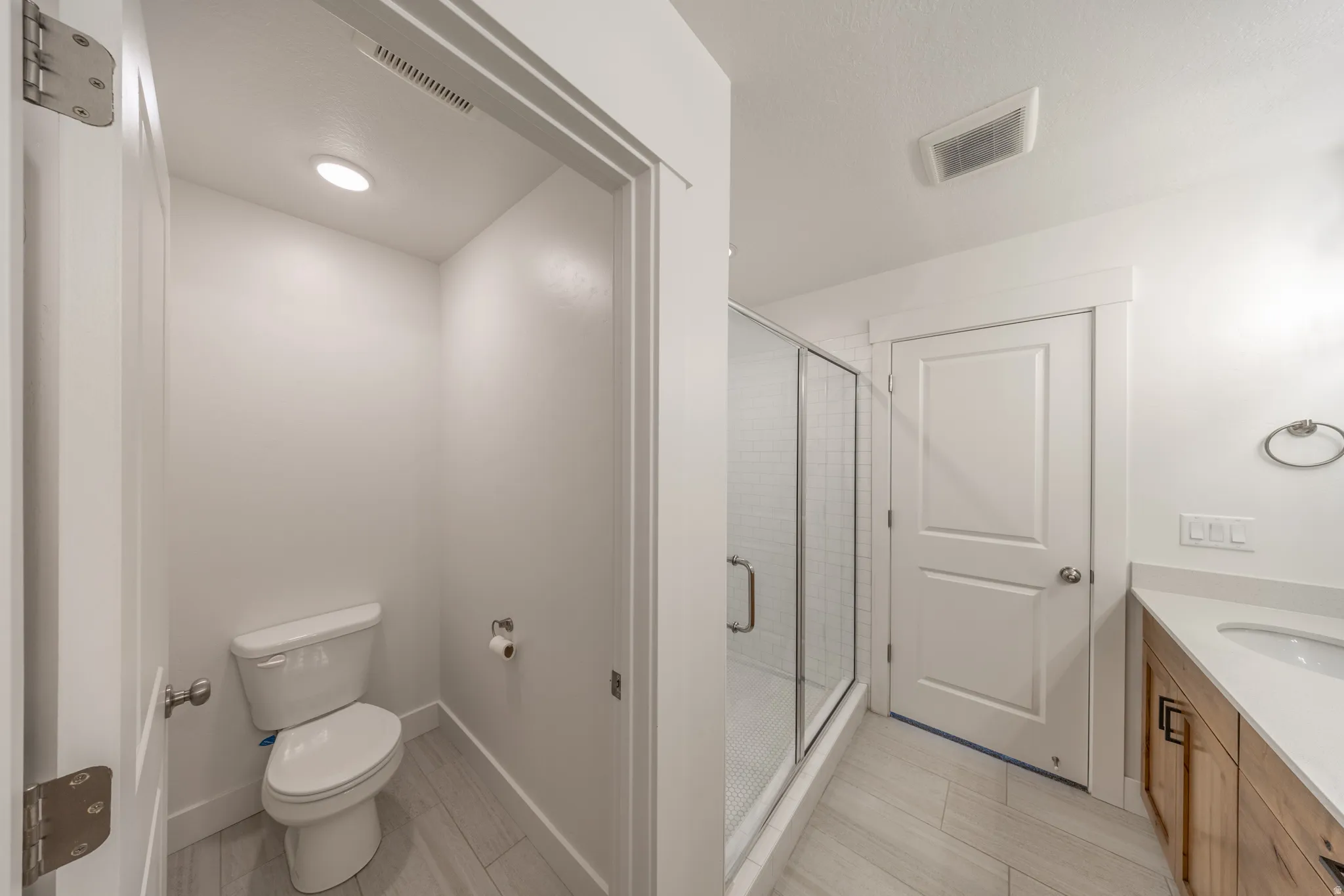 Bathroom featuring a glass-enclosed shower, wood-finish vanity, light-toned countertop, and recessed lighting