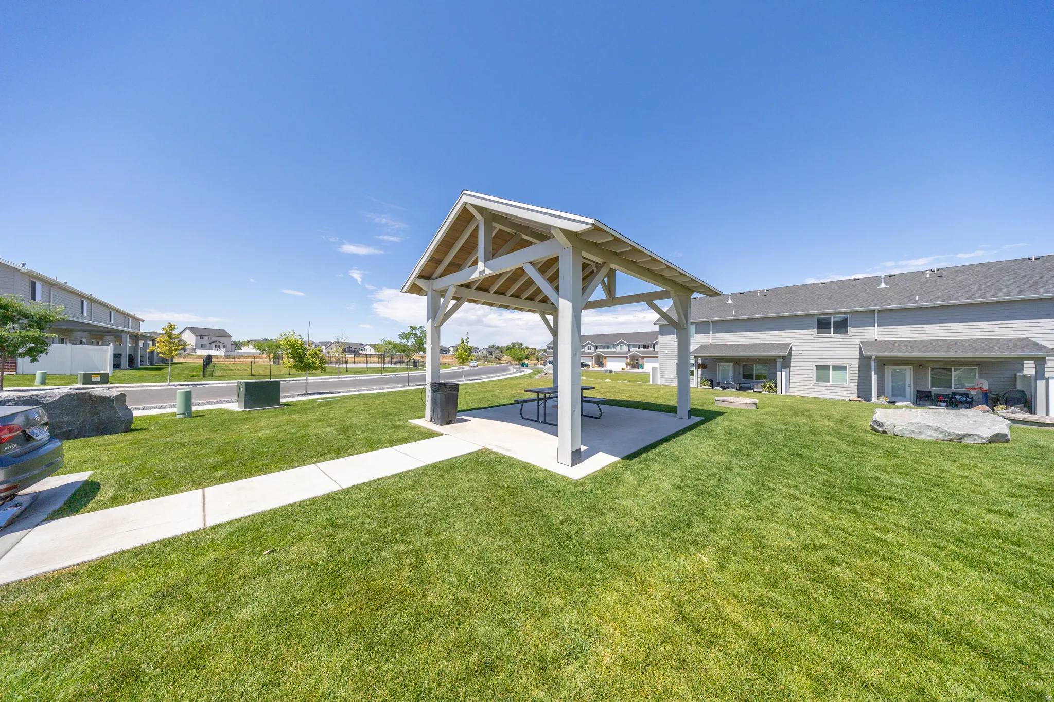 Covered outdoor pavilion with concrete pad, surrounded by a manicured lawn and mature landscaping