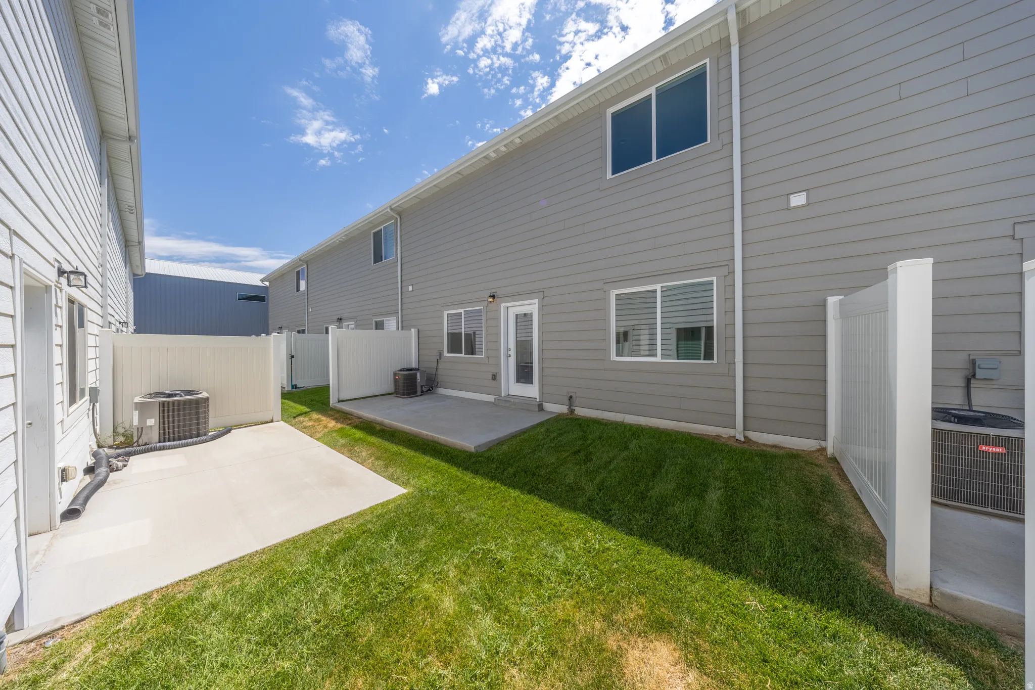 Rear property exterior featuring gray horizontal siding, a ground-level patio, and a white vinyl privacy fence