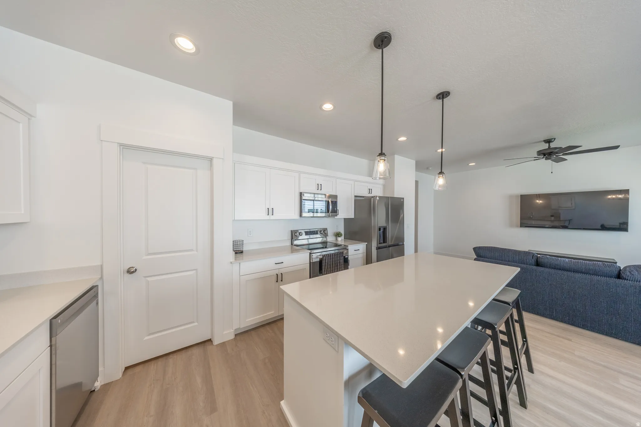 Light-filled kitchen featuring a large island with seating, stainless steel appliances, white cabinetry, recessed lighting, and wood-finish flooring
