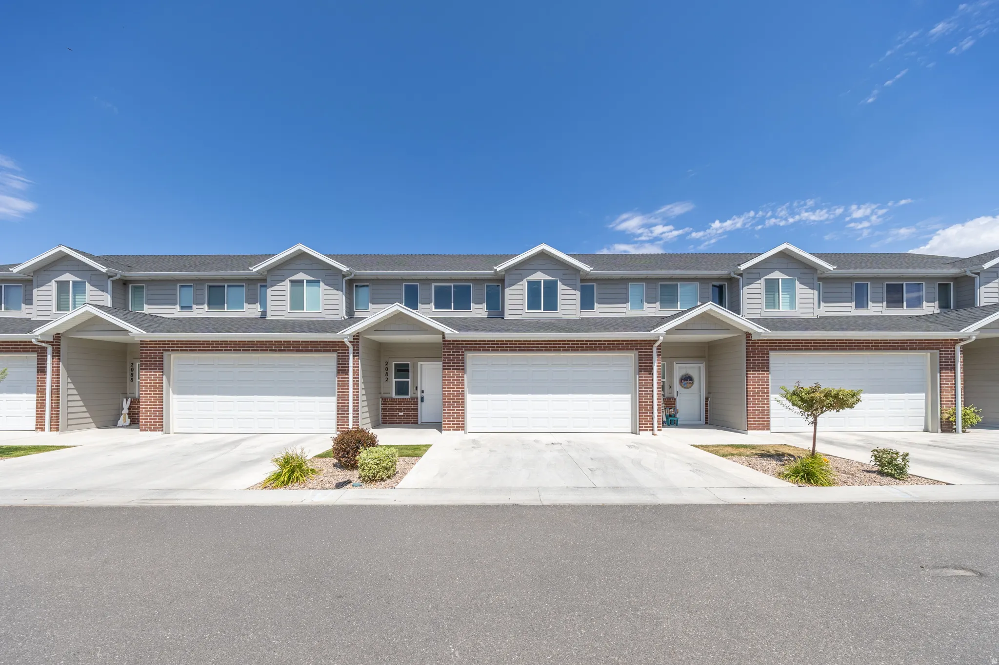 Modern townhome exterior featuring light gray siding, red brick accents, individual attached garages, and concrete driveways