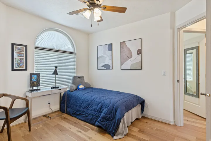 Room featuring wood-finish flooring, an arched top window with blinds, and a ceiling fan
