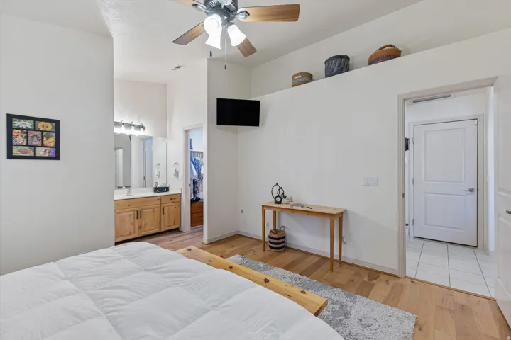 Bedroom featuring wood-finish flooring, a ceiling fan, and a light-toned wood vanity with a dual-sink countertop and wall-mounted lighting