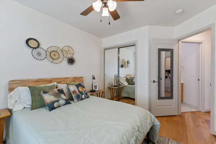 Room featuring wood-finish flooring, a ceiling fan with light fixture, mirrored sliding closet doors, and a white paneled door