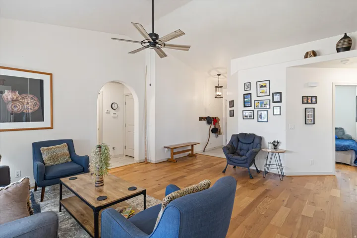 Living area featuring high vaulted ceilings, light wood-finish flooring, an arched entryway, and a ceiling fan with light fixture