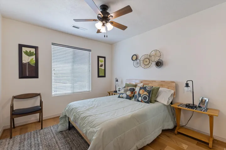 Bedroom featuring light wood-finish flooring, a ceiling fan with integrated lighting, a window with horizontal blinds, and neutral wall tones