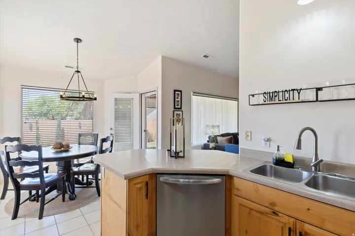 Kitchen featuring a stainless steel double basin sink with a pull-down faucet, light-toned countertops, natural wood-finish cabinetry, and a built-in stainless steel dishwasher