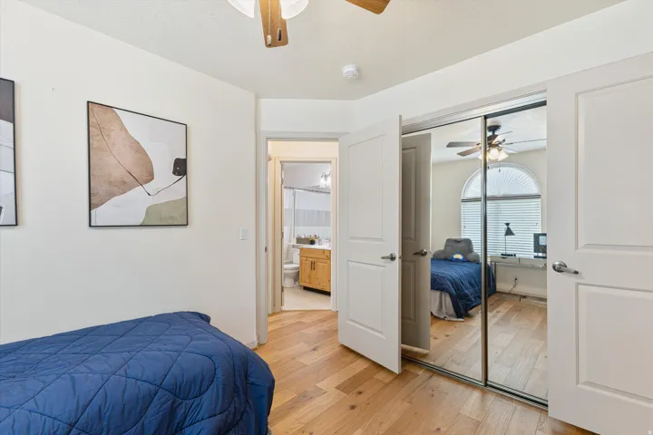 Bedroom featuring wood-finish flooring, a ceiling fan with integrated lighting, and a mirrored sliding closet door