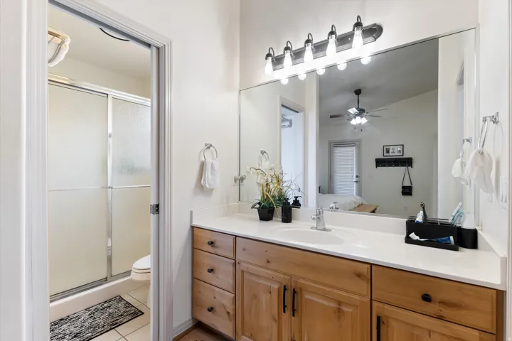Bathroom featuring a light wood-finish vanity with a single sink and white countertop, full-width mirror, and a five-bulb vanity light fixture