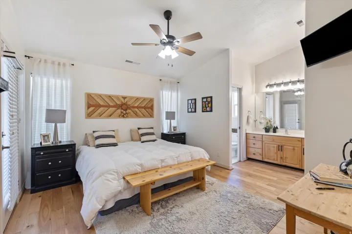Expansive bedroom featuring wood-finish flooring, a ceiling fan, and multiple windows with sheer white curtains