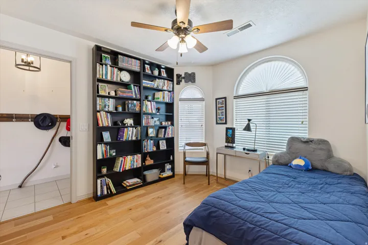 Arched window with blinds, wood-finish flooring, built-in shelving, ceiling fan, and recessed lighting