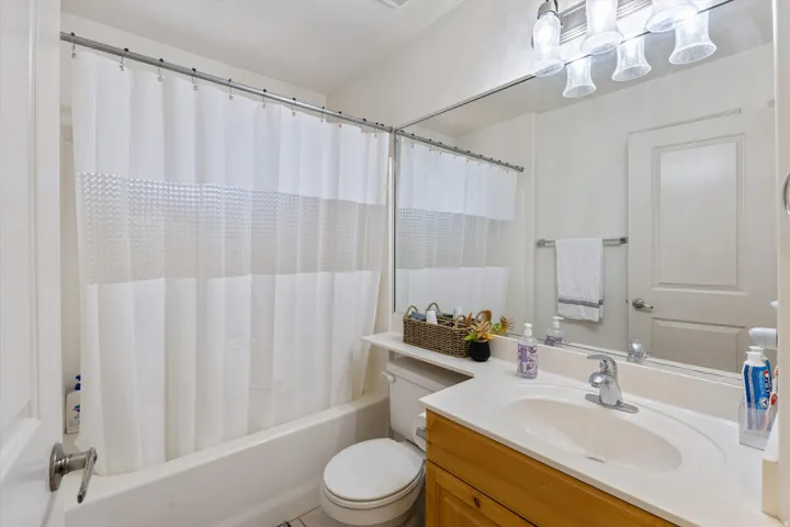 Bathroom featuring a built-in tub with shower, wood-finish vanity with an integrated sink and countertop, large wall-mounted mirror, and a four-bulb vanity light fixture