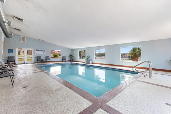 Indoor swimming pool featuring a sloped ceiling with exposed ductwork, multiple windows, and a surrounding textured deck with a brick-patterned border