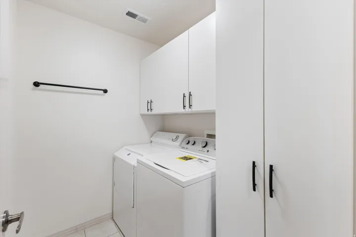 Dedicated laundry area featuring white cabinetry with black hardware, an overhead storage cabinet, and a full-height pantry-style cabinet
