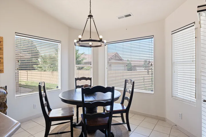 Dining area featuring a contemporary chandelier, multiple windows with blinds, a vaulted ceiling, and tile flooring