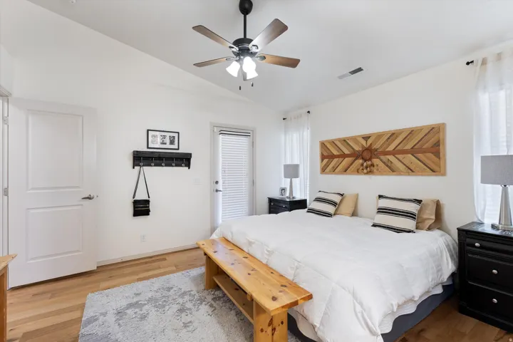 Bedroom featuring light wood-finish flooring, a ceiling fan with light fixture, white walls, and a door with external access