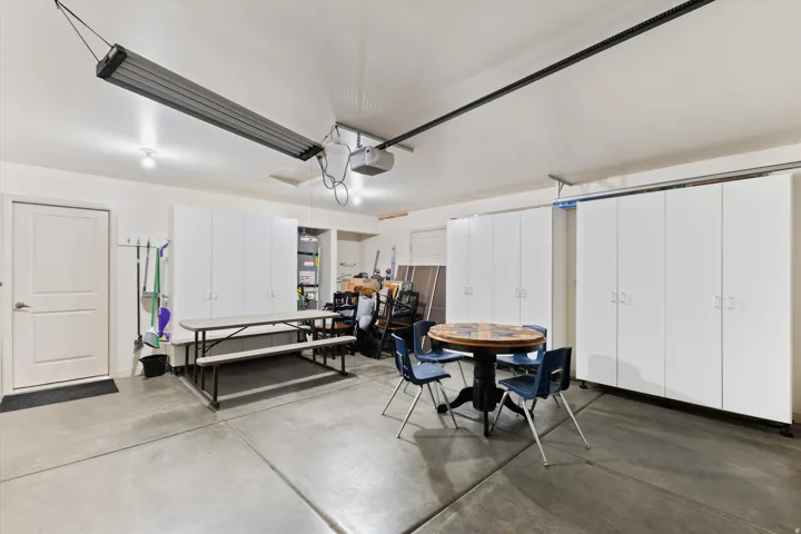 Spacious garage featuring extensive built-in white cabinetry, concrete flooring, overhead lighting, and a suspended lighting fixture
