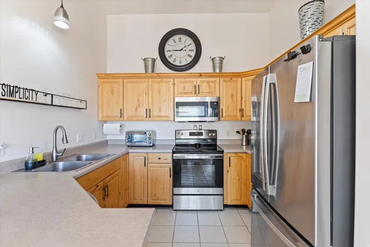 Kitchen featuring wood-finish cabinetry, stainless steel appliances, a double basin sink, and light-toned countertops