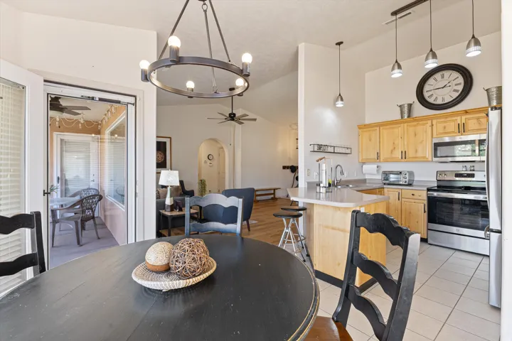 Open-concept kitchen and dining area featuring light wood cabinetry, stainless steel appliances, a kitchen island with seating, a large circular dining table, and direct access to an enclosed patio