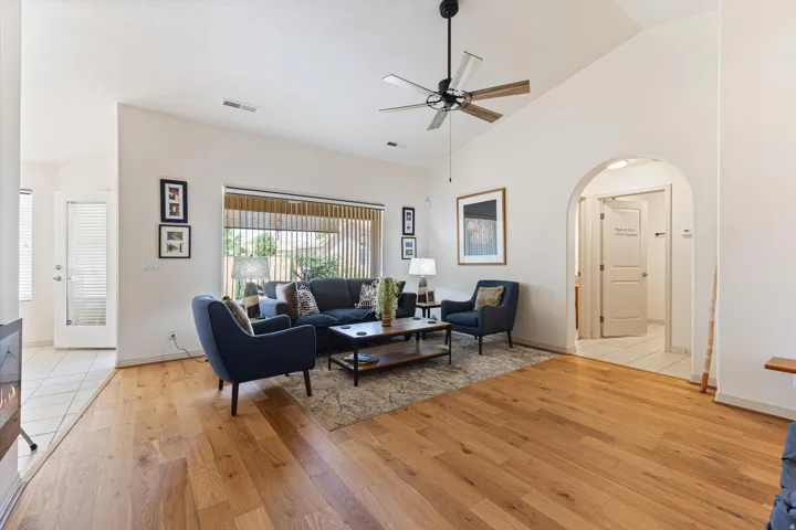 Spacious living area featuring wood-finish flooring, vaulted ceilings, and a large picture window with vertical blinds