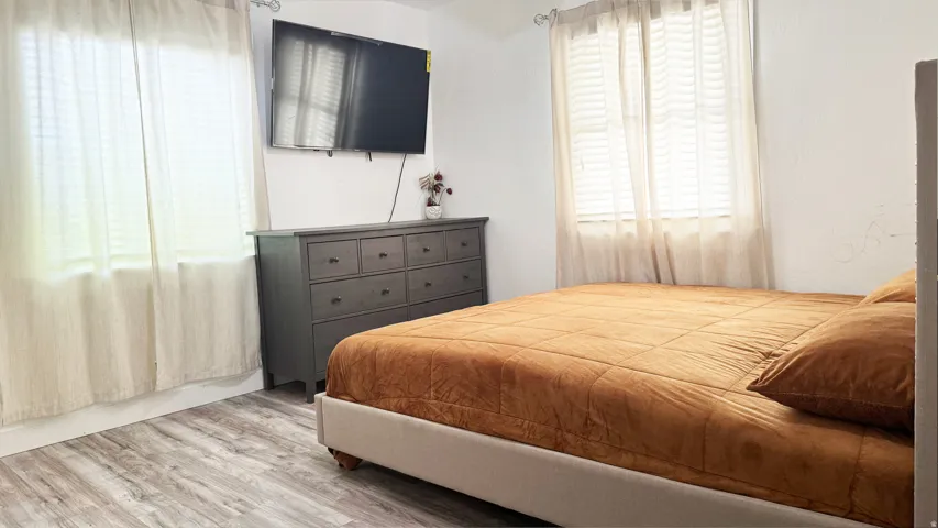Room featuring two windows with blinds and sheer curtains, wood-finish flooring, and white baseboards