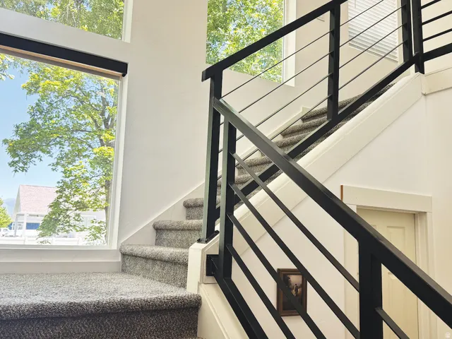 Stairwell featuring modern black metal balusters, gray carpeted steps, and large windows with integrated blinds