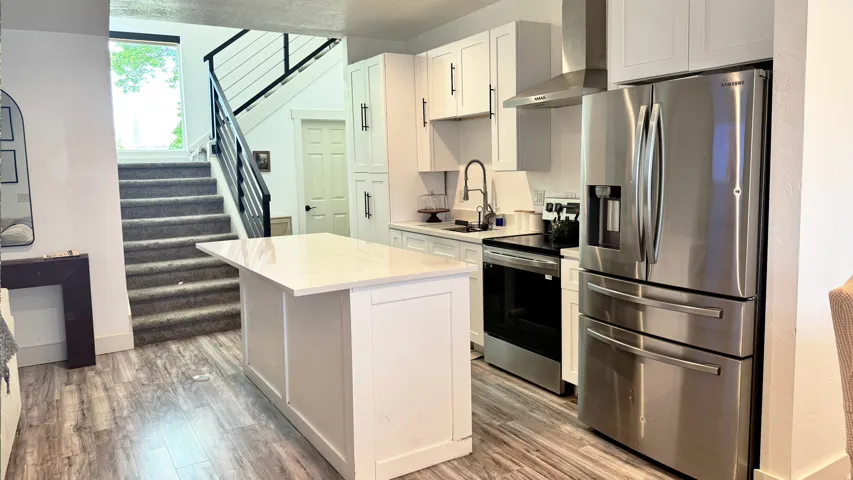Open-concept kitchen featuring white cabinetry, stainless steel appliances, a center island with a light-colored countertop, and wood-finish flooring