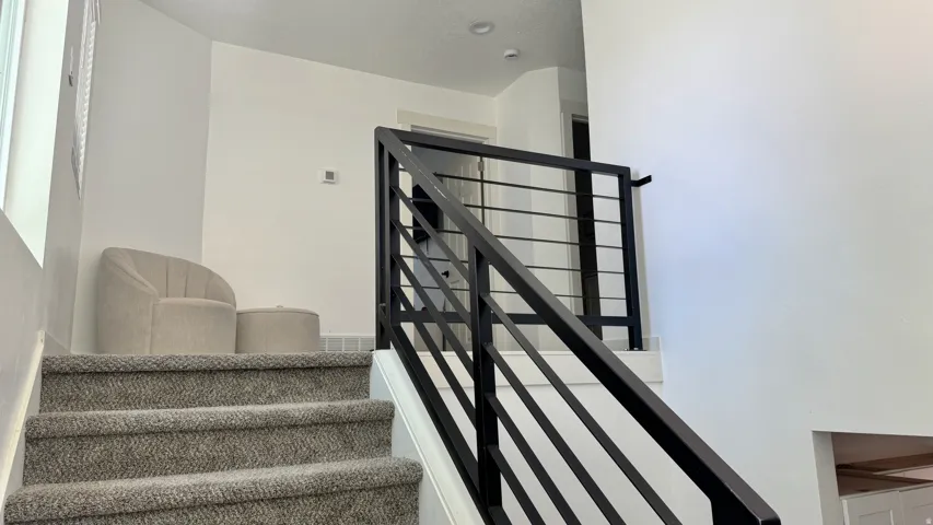 Staircase featuring dark-finish horizontal metal railings, gray carpeted treads, and bright white walls