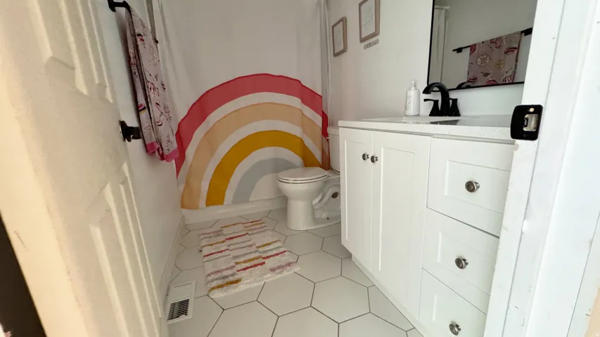 Bathroom featuring white hexagonal floor tiles, a white vanity with shaker-style cabinetry, a light-toned countertop, and a black-finish faucet