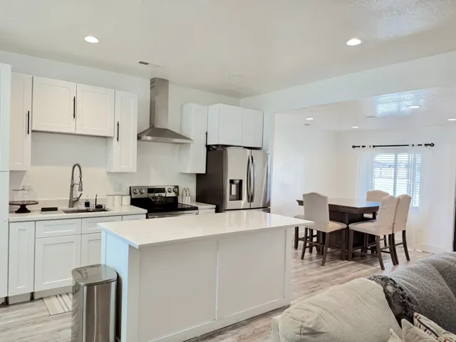 Open-concept kitchen featuring white shaker cabinetry, stainless steel appliances, a center island with a light-toned countertop, and recessed lighting