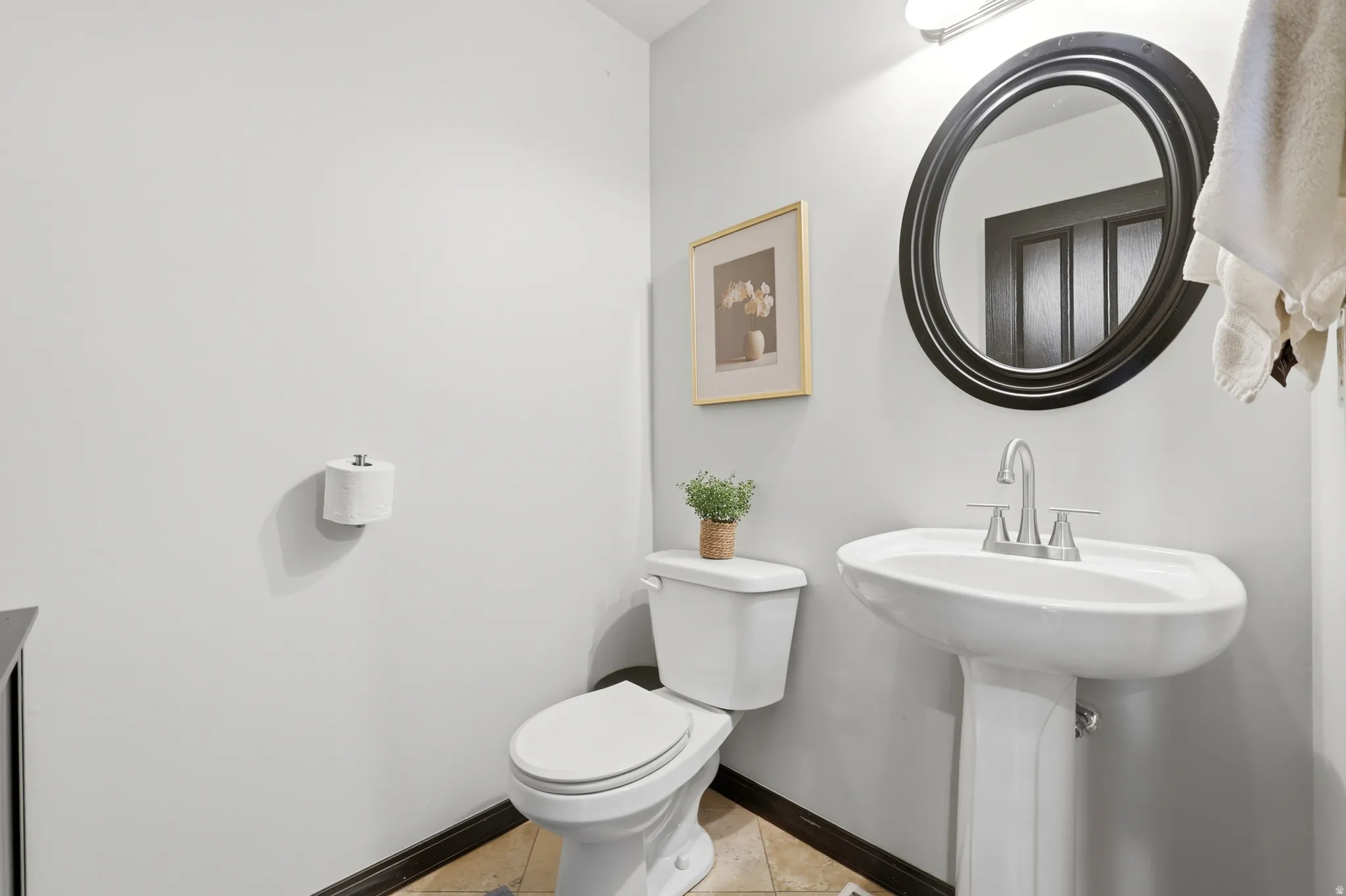 Pedestal sink with chrome faucet, circular framed mirror, and light gray wall paint