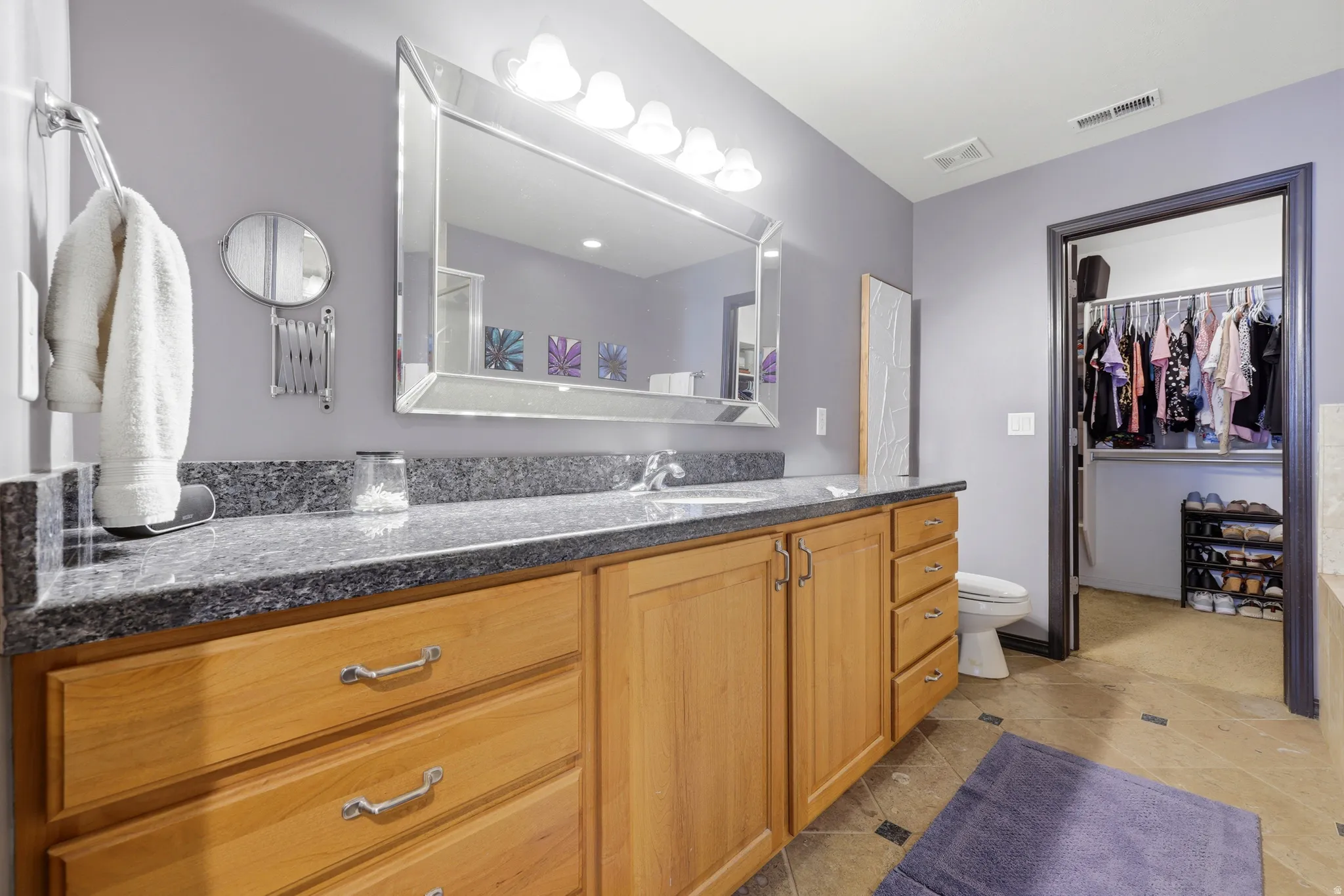 Bathroom vanity featuring wood-finish cabinetry, a stone countertop, and a large framed mirror with integrated lighting
