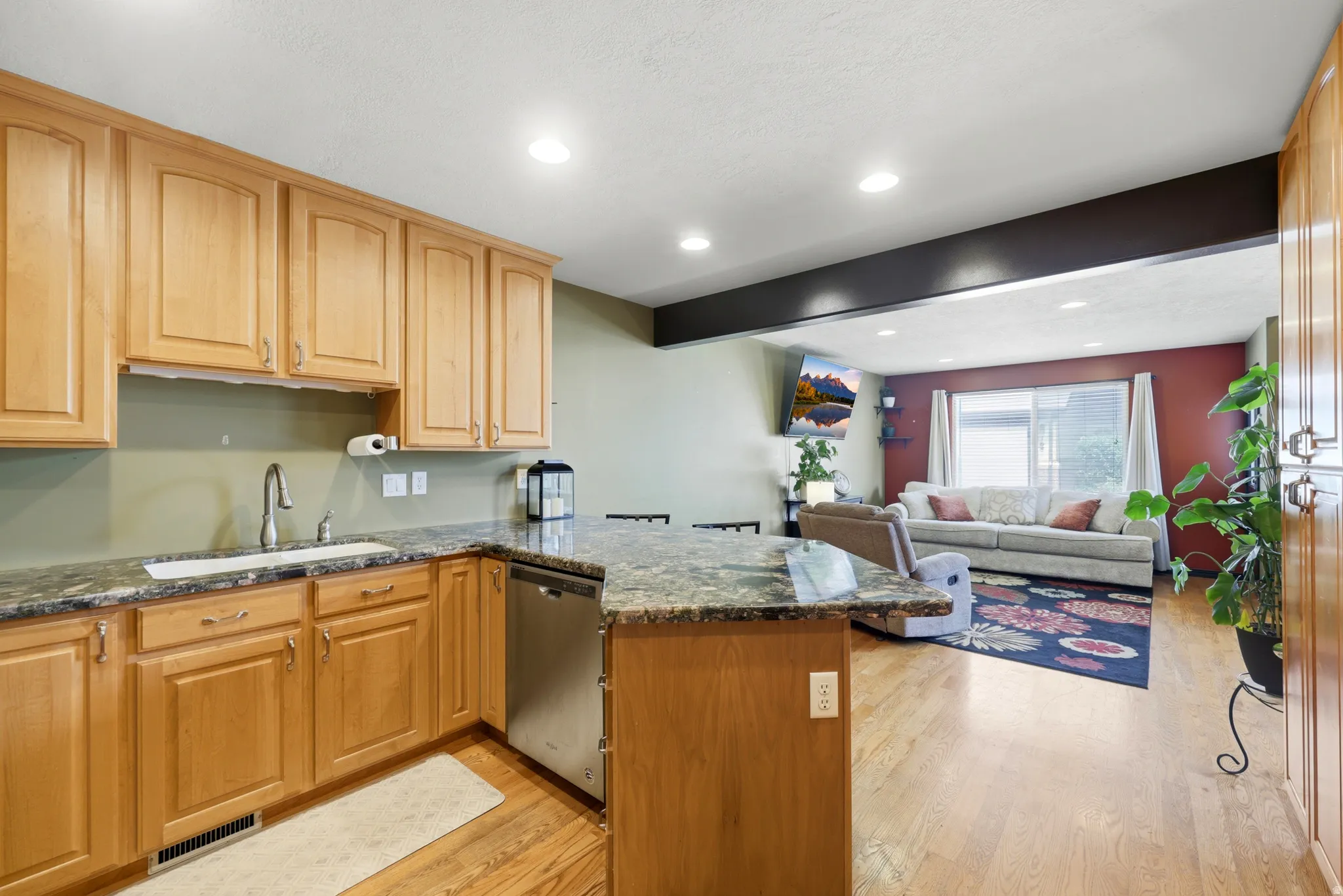 Kitchen featuring light wood cabinetry, granite countertops, an undermount sink with a gooseneck faucet, and stainless steel dishwasher