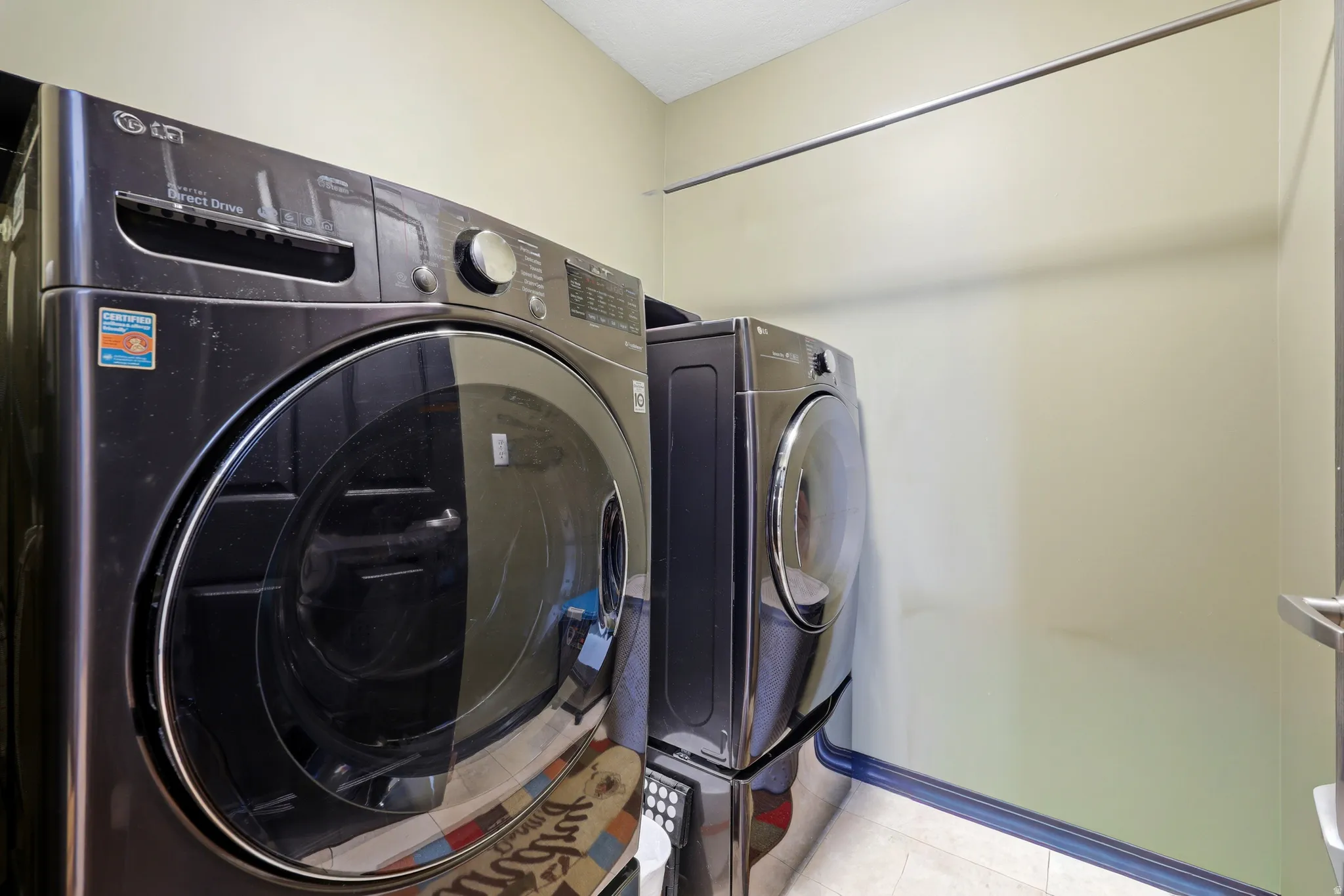 Dedicated laundry area featuring a dark gray front-loading washer and dryer set, a high-mounted metal hanging rod, light-toned walls, and a light-toned floor