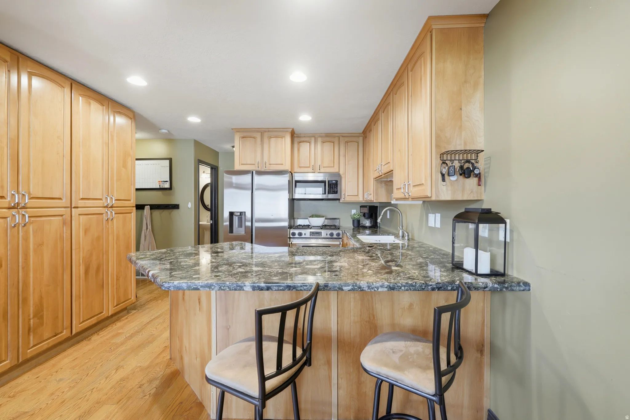 Kitchen featuring an integrated breakfast bar with a stone-look countertop, wood-finish cabinetry, stainless steel appliances, recessed lighting, and wood-finish flooring